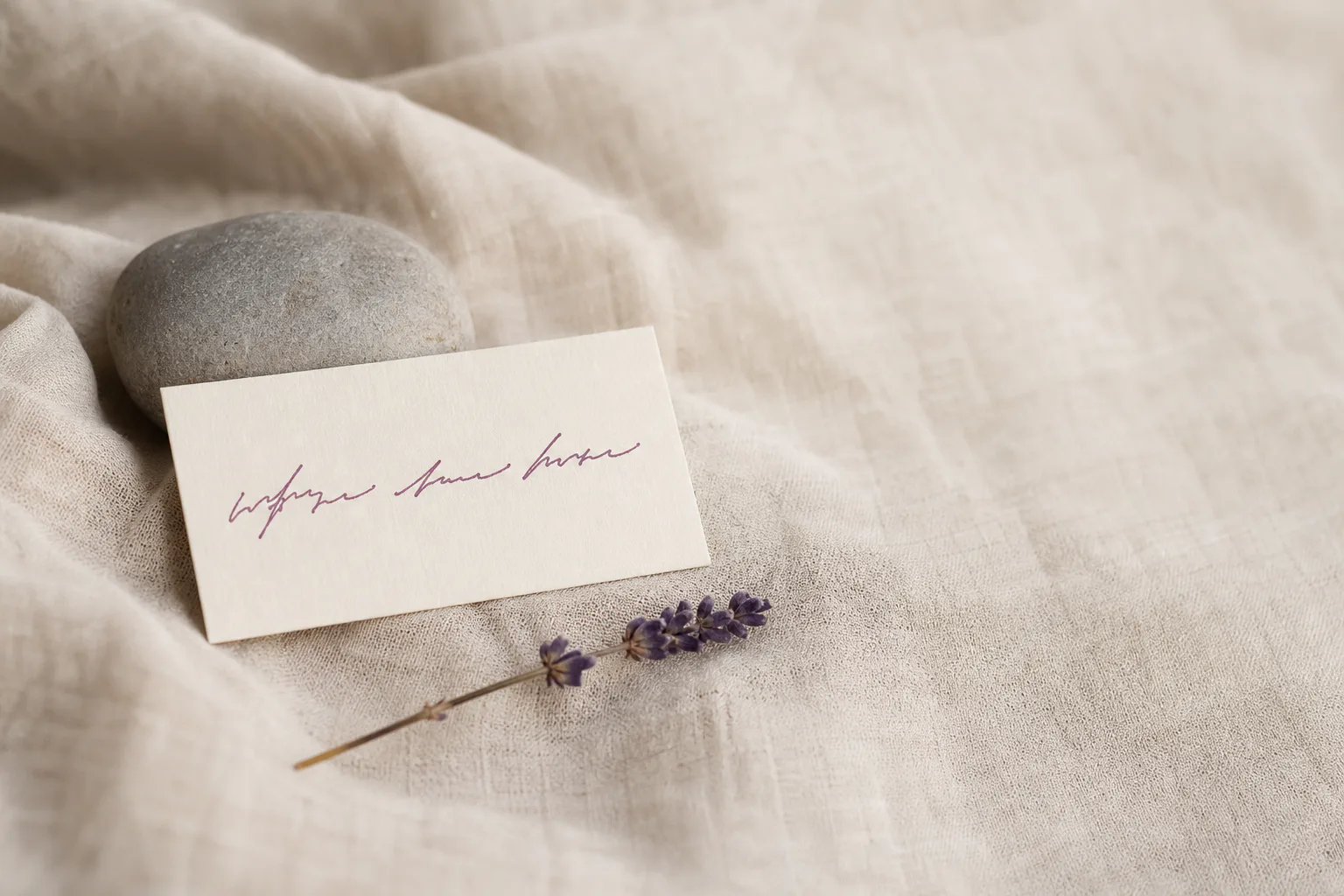 Small handwritten affirmation card resting against a smooth river stone on linen.