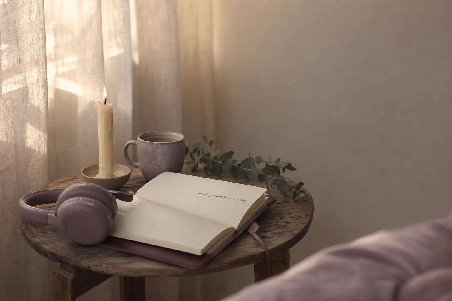 Soft morning light over a small table with headphones, an open journal, a half-burnt taper candle, and a sprig of eucalyptus.